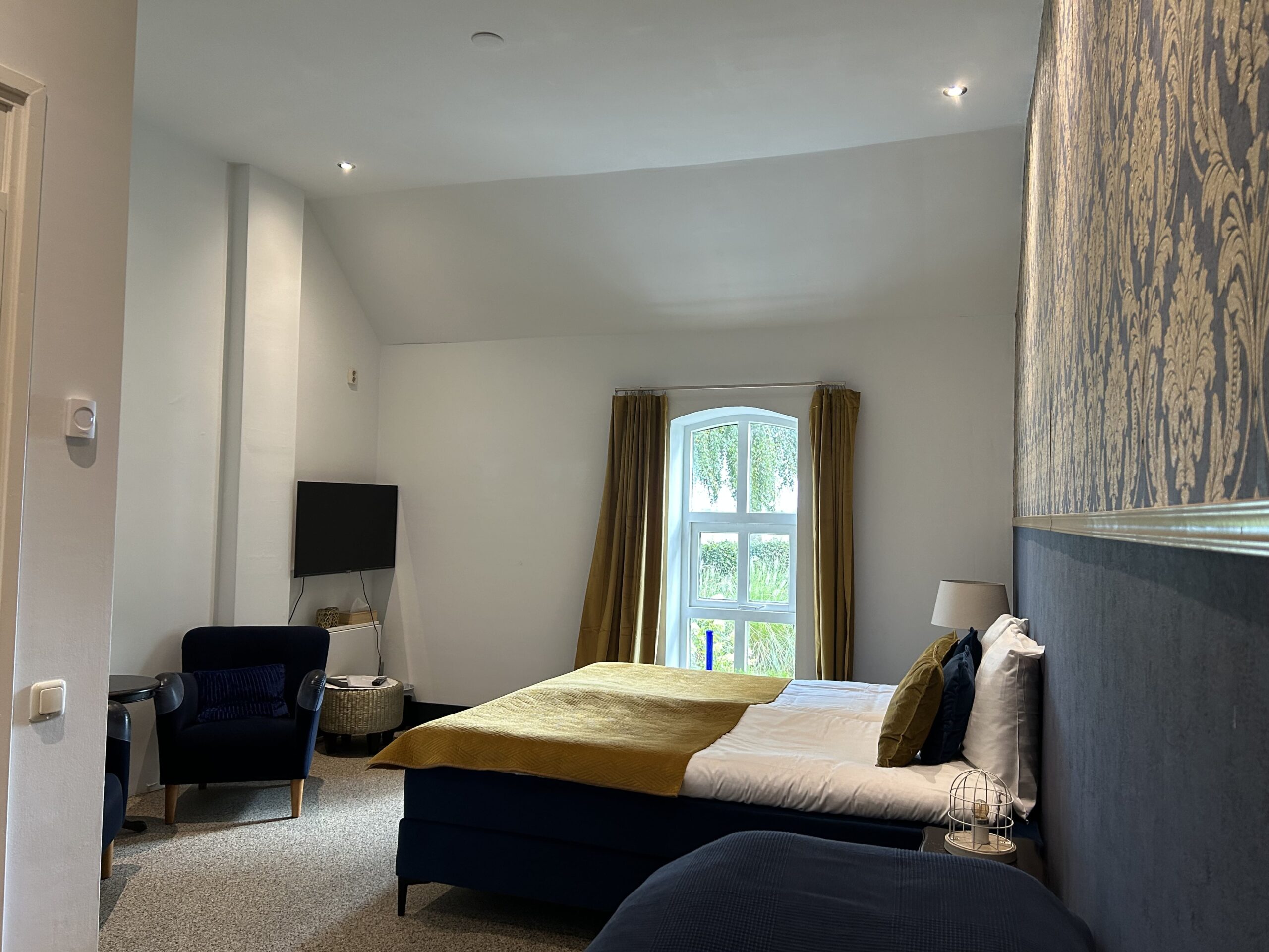 Sfeervolle boutique hotelkamer op Mariafarm met een boogvenster en uitzicht op het groen